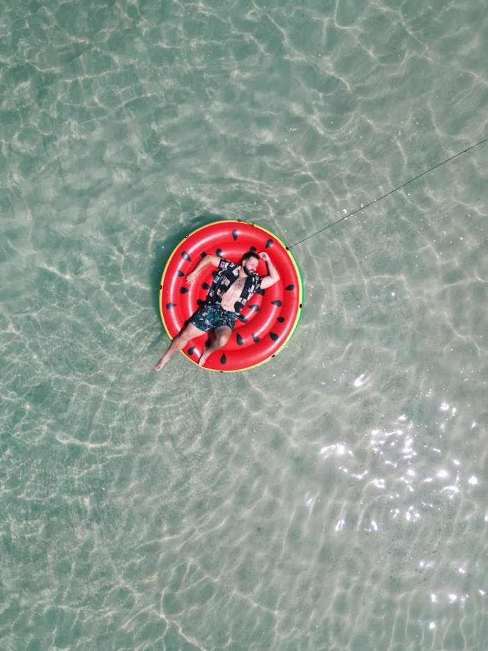 A relaxing summer day with a man floating on a watermelon inflatable in clear ocean water.