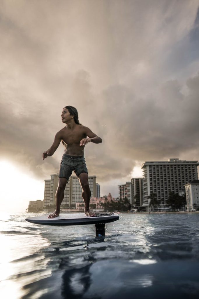 A man rides an electric surfboard near a beachfront hotel during sunset. Perfect depiction of modern surfing lifestyle.