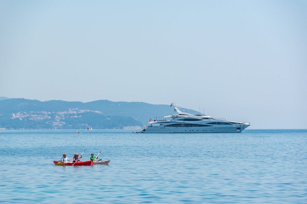 A serene scene of a luxury yacht and kayaking on a calm blue sea under a clear sky.
